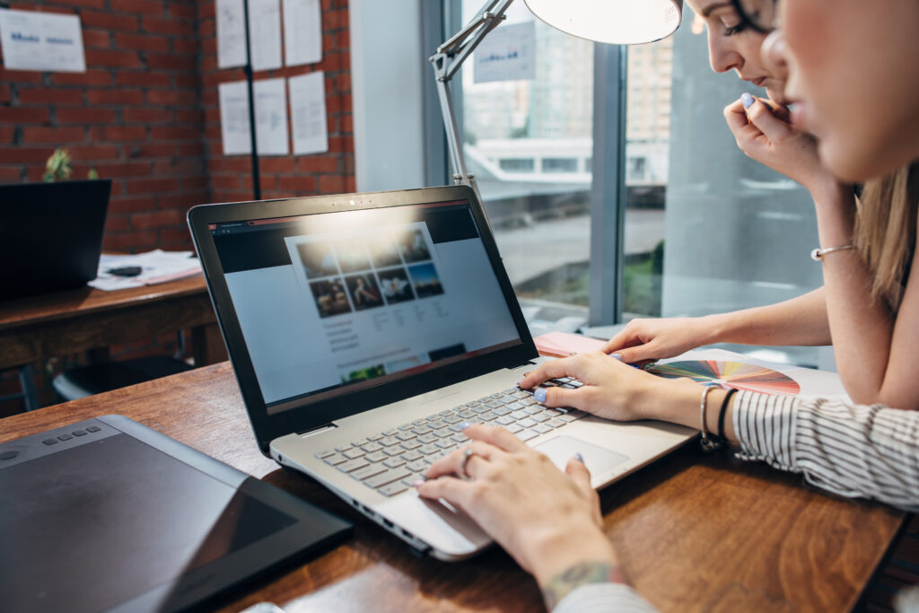 Two women working on new website design choosing pictures using the laptop surfing the internet.