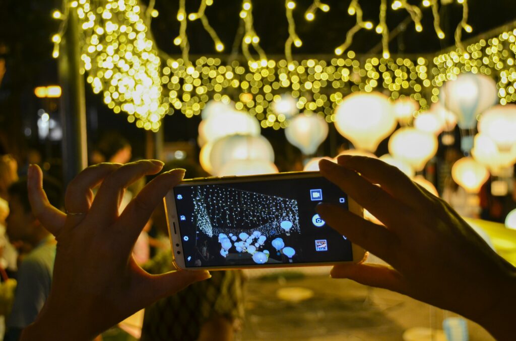 woman holding phone up to take photo of lanterns and fairy lights